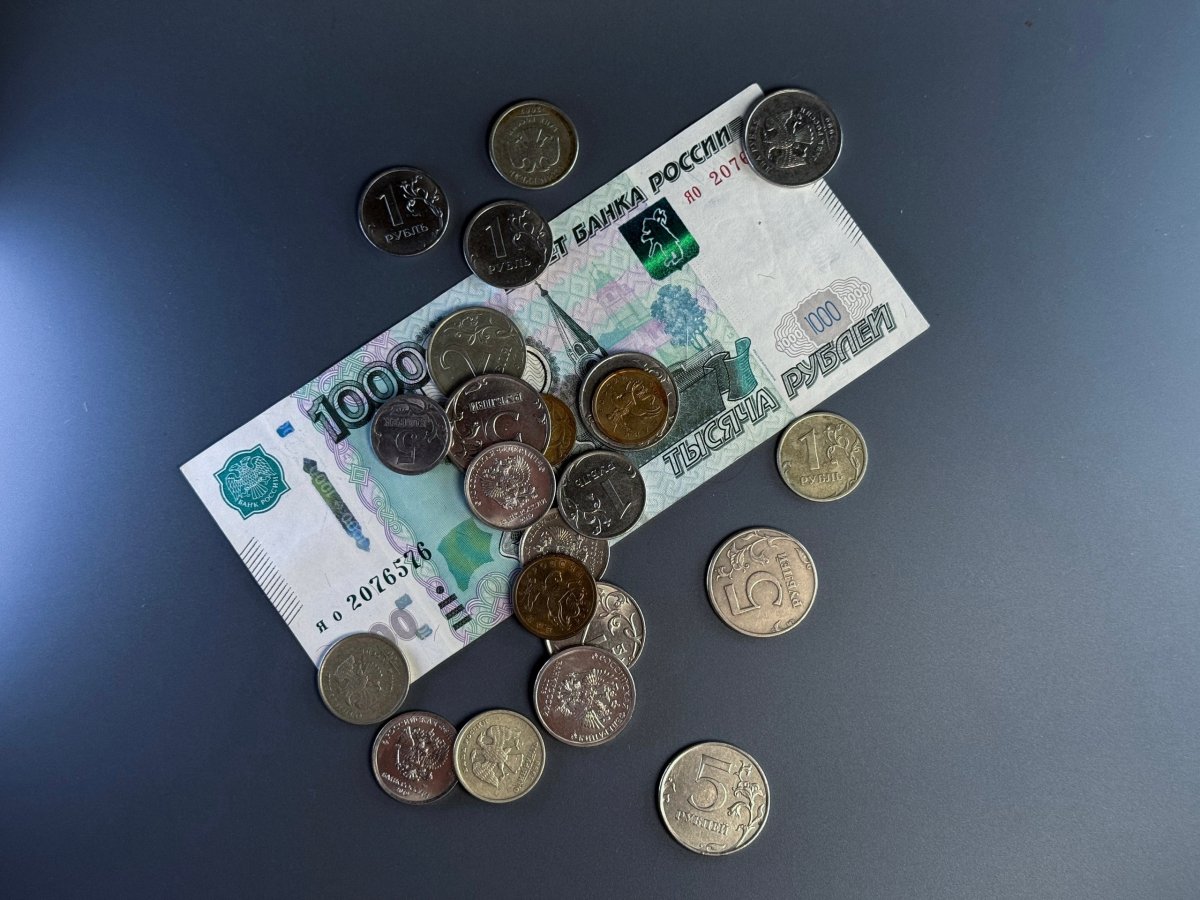 Монеты и купюра номиналом 1000 рублей лежат на столе.