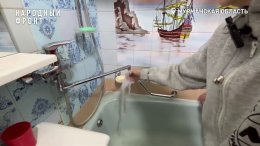 Человек трогает рукой воду из-под крана в ванной комнате.