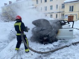 Пожарный тушит горящий автомобиль во дворе дом зимой в Мурманске.