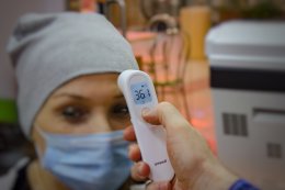 Женщине в маске измеряют температуру электронным термометром.