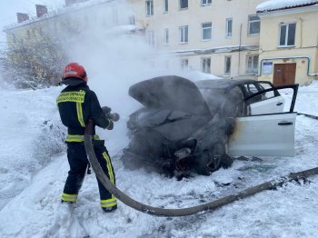 Пожарный тушит горящий автомобиль во дворе дом зимой в Мурманске.