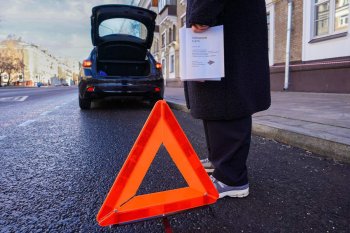 Автомобильный аварийный знак на фоне человека и поднятой двери багажника автомобиля.