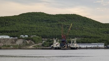 Левый, западный берег Кольского залива в Мурманской области с двумя стоящими на причале судами.