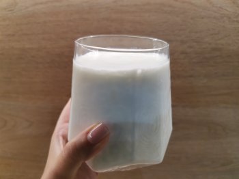 Рука держит стеклянный стакан с молочным продуктом.