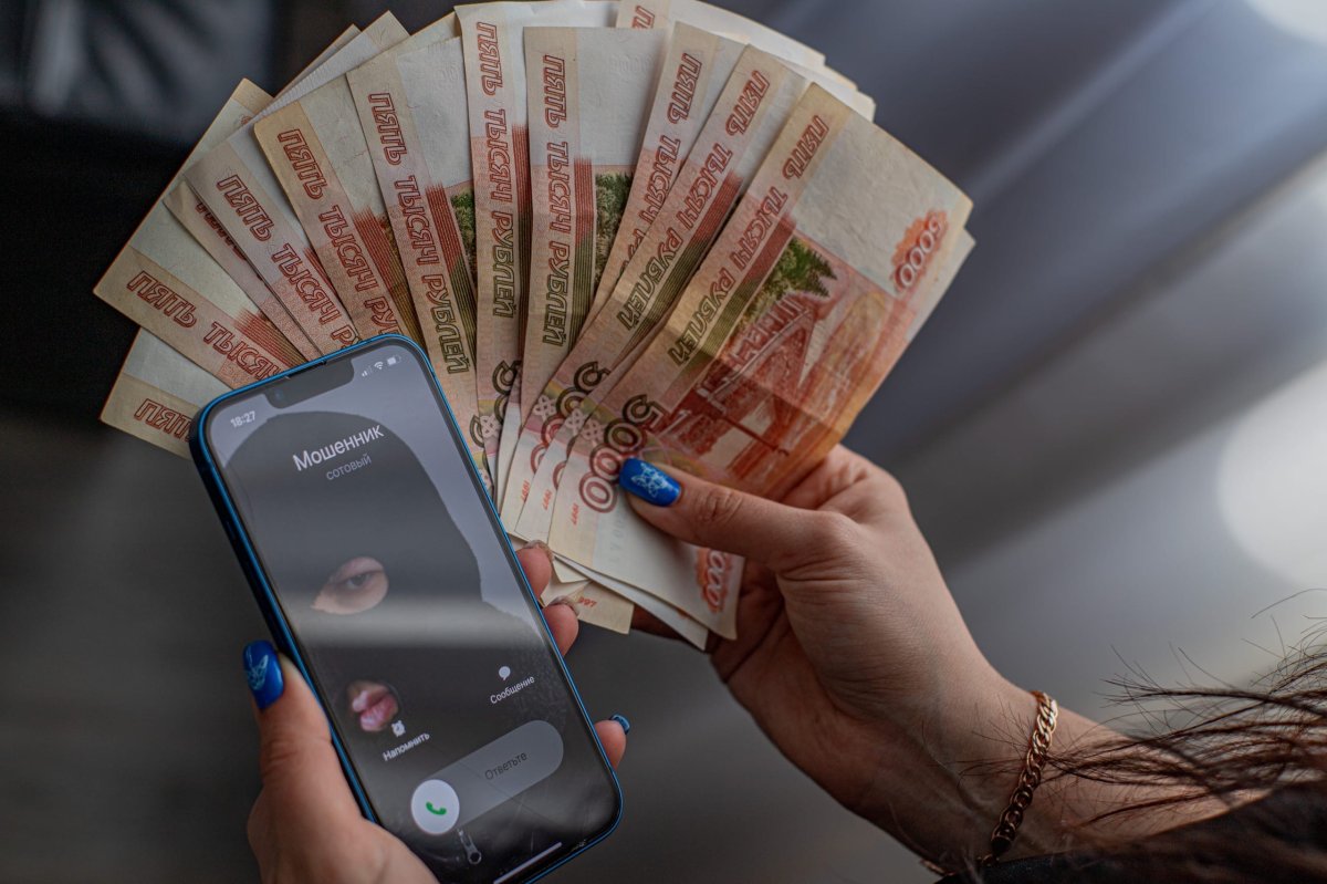 В женских руках телефон с изображением мошенника и денежные купюры
