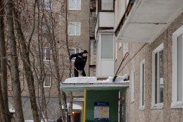 Рабочий чистит козырек подъезда от снега в Мурманске