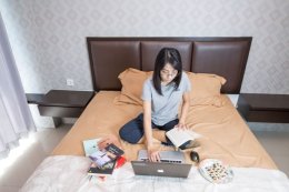 девушка работает на ноутбуке, сидя на кровати