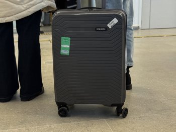 Ноги в брюках и рядом чемодан на колесах.