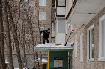 Рабочий чистит козырек подъезда от снега в Мурманске