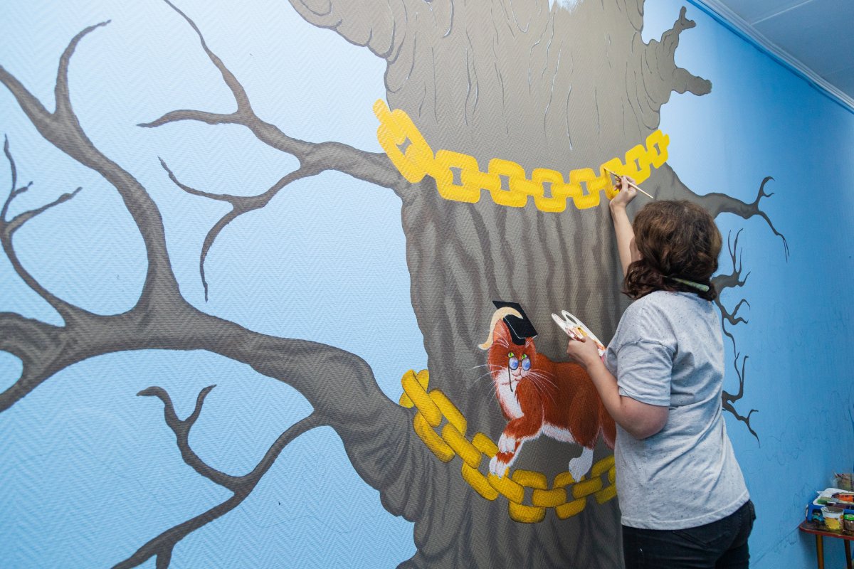Художница раскрашивает стену в детском саду