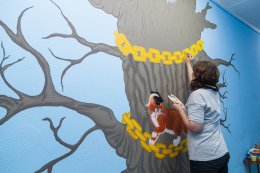 Художница раскрашивает стену в детском саду