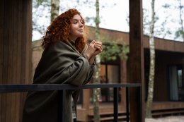 Девушка укуталась в плед и стоит на террассе.