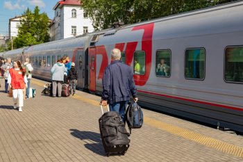 Человек с чемодааном на перроне вокзала идёт к поезду.