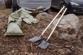 Лопаты и мешки для мусора лежат на земле.