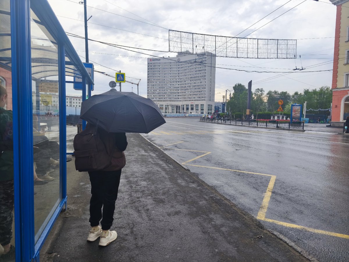 Человек с зонтом стоит на остановке.
