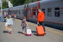Мужчина с детьми везут чемоданы по перрону к поезду.