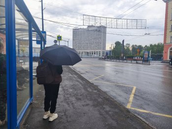 Человек с зонтом стоит на остановке.